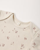 Close-up of a cream-colored ribbed knit garment, likely a baby top or sweater, featuring a delicate brown floral and leaf pattern scattered across the fabric.