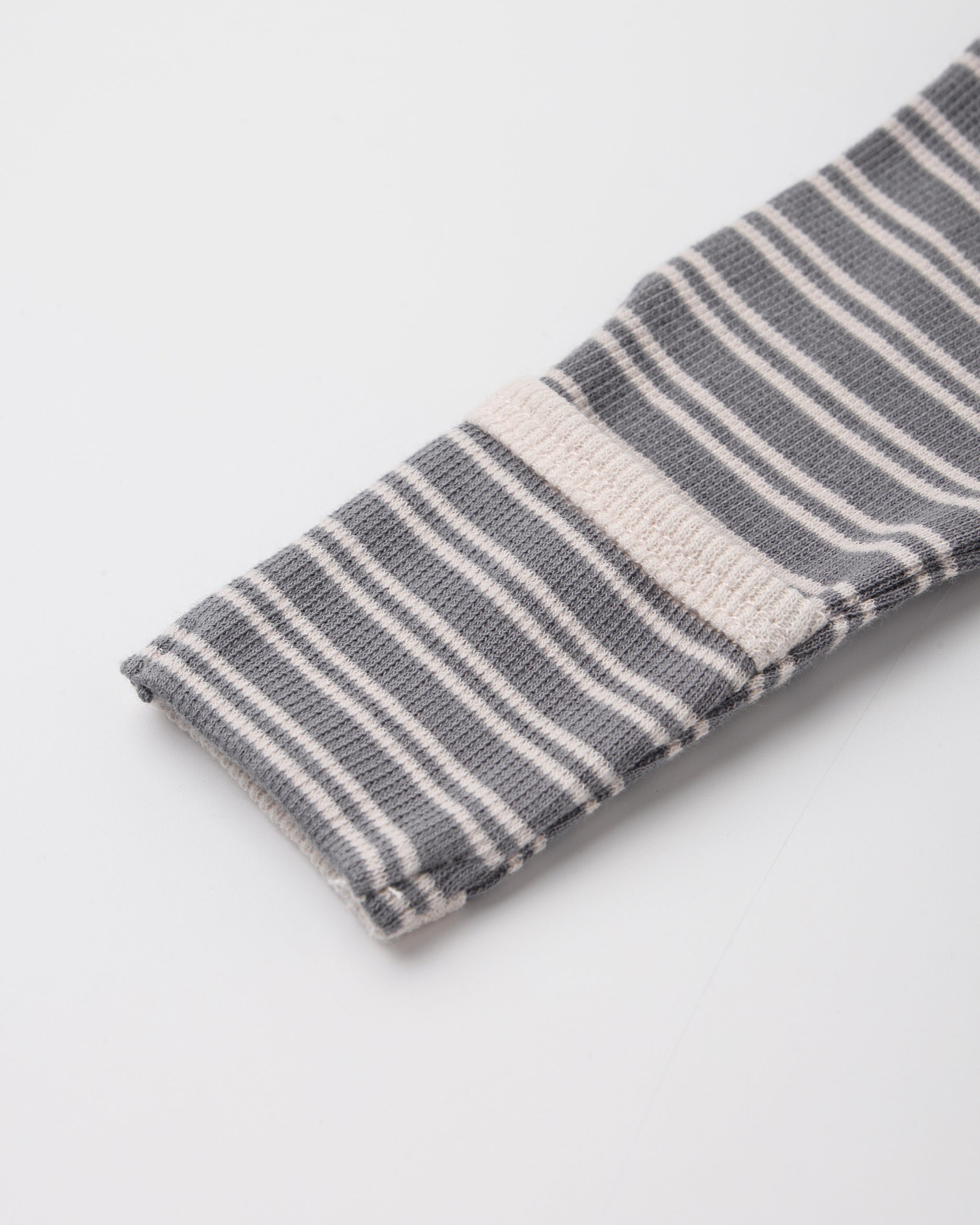 A close-up of a folded knit fabric item, likely a sock or sleeve cuff, featuring a gray and white striped pattern with a solid white stripe accent, on a light gray background.