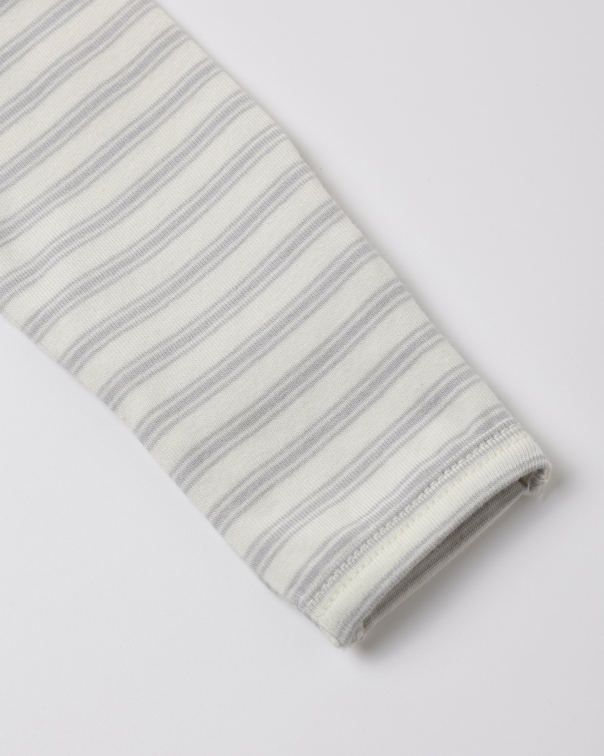 A close-up of a folded knit fabric sleeve or cuff with thin gray horizontal stripes on an off-white background, shown on a light gray studio background.