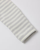 A close-up of a folded knit fabric sleeve or cuff with thin gray horizontal stripes on an off-white background, shown on a light gray studio background.