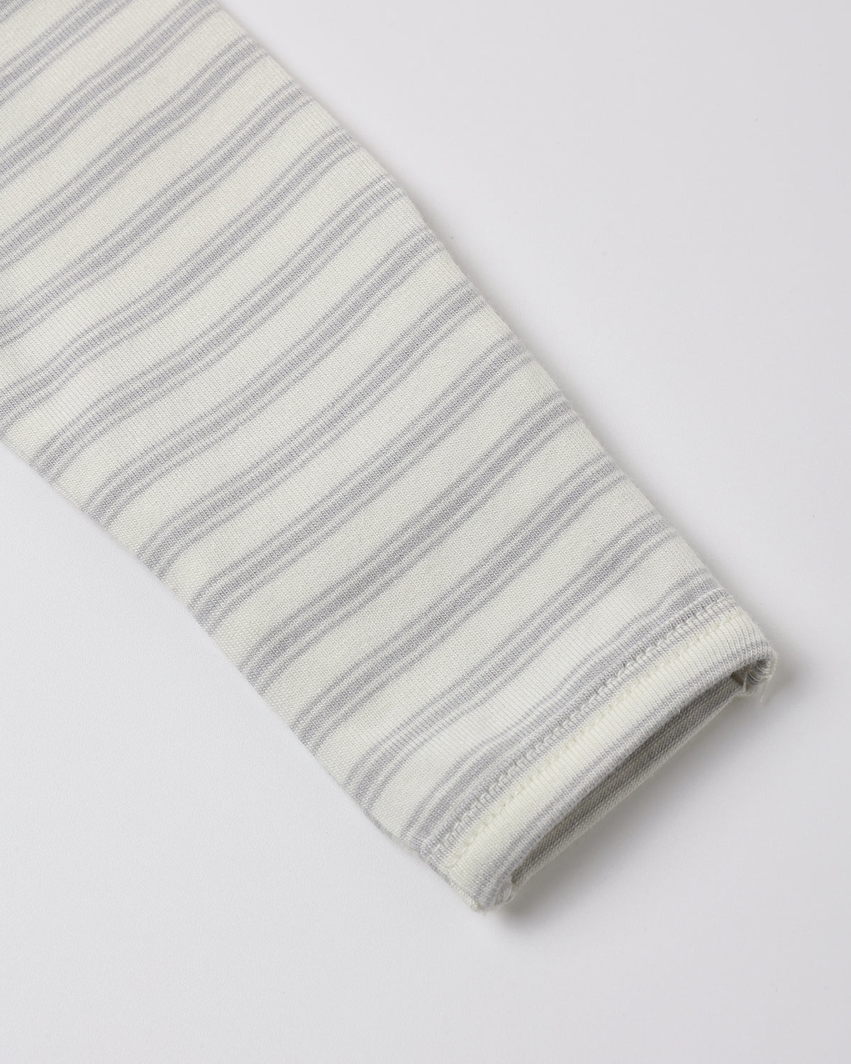 A close-up of a folded knit fabric sleeve or cuff with thin gray horizontal stripes on an off-white background, shown on a light gray studio background.