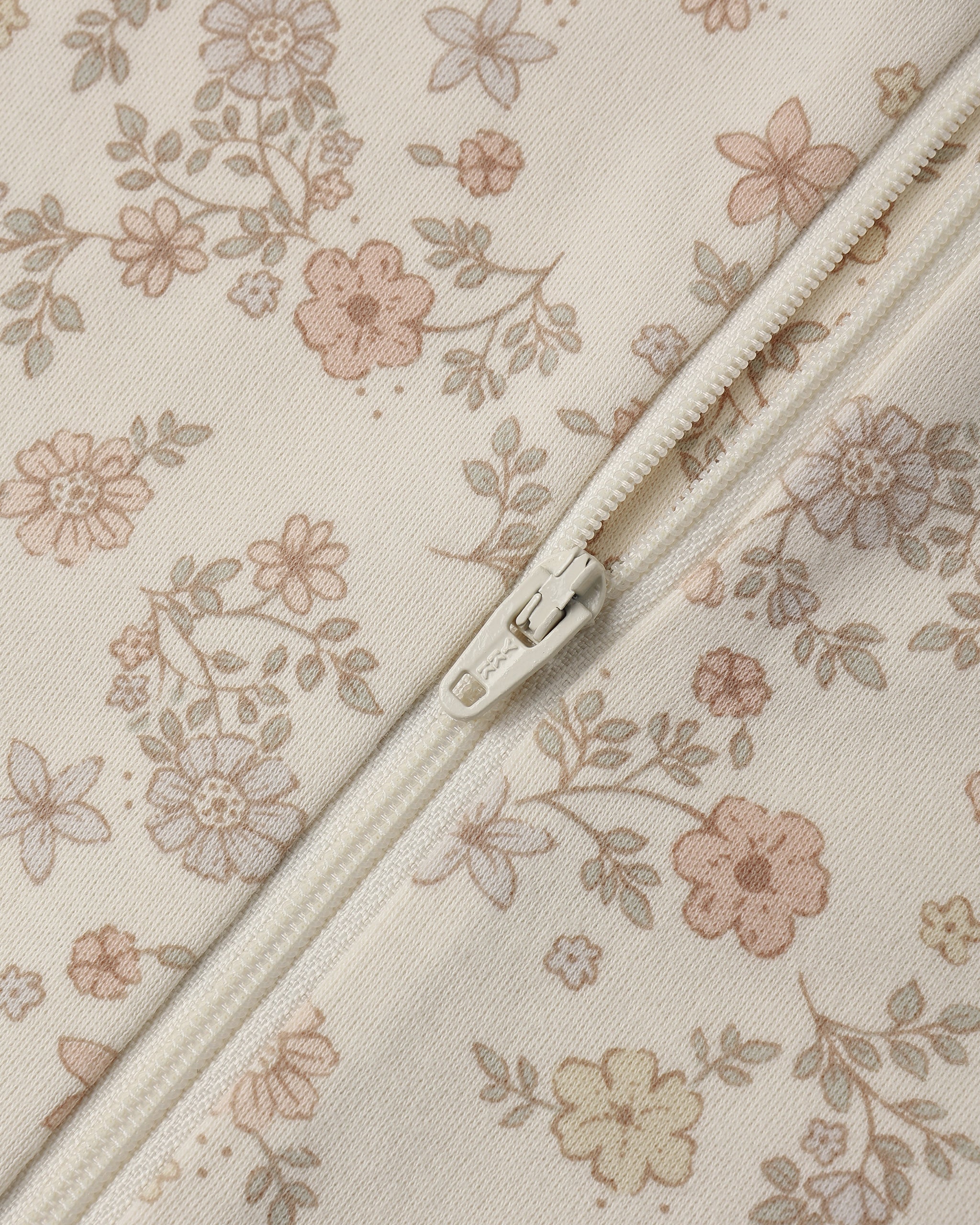Close-up of a cream-colored fabric with a delicate pink and beige floral print, featuring a matching cream zipper running diagonally across the frame.