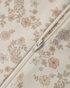 Close-up of a cream-colored fabric with a delicate pink and beige floral print, featuring a matching cream zipper running diagonally across the frame.