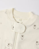 Close-up of a baby garment in warm off-white/cream with a small sheep print and a snap-button closure at the neckline.