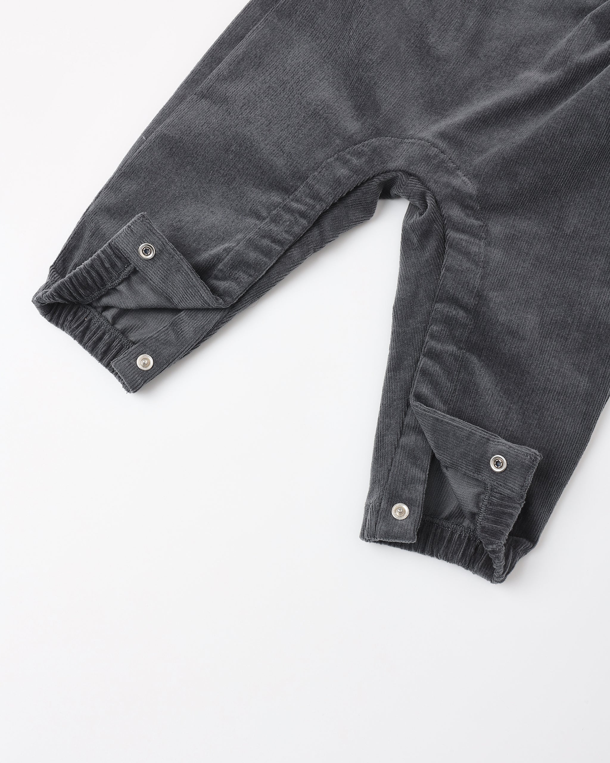 Close-up of dark gray corduroy pants with buttoned cuff details, laid flat on a white background.