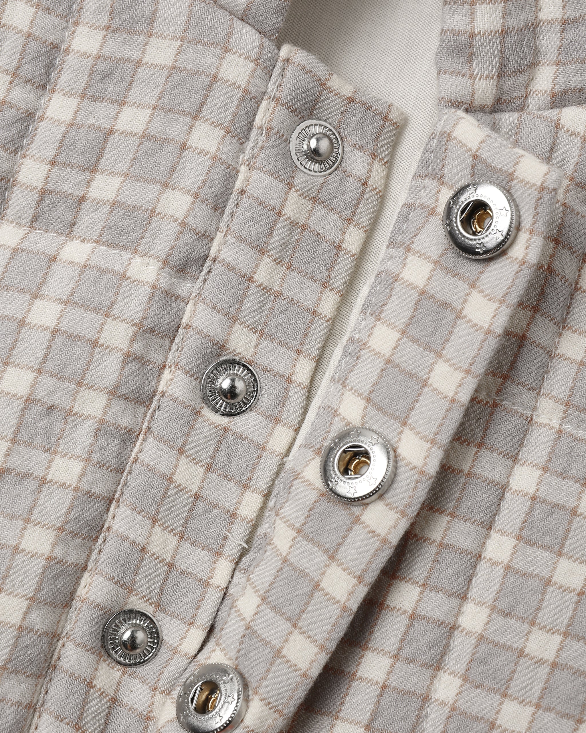 Close-up of a light gray and cream gingham plaid shirt with silver snap buttons.