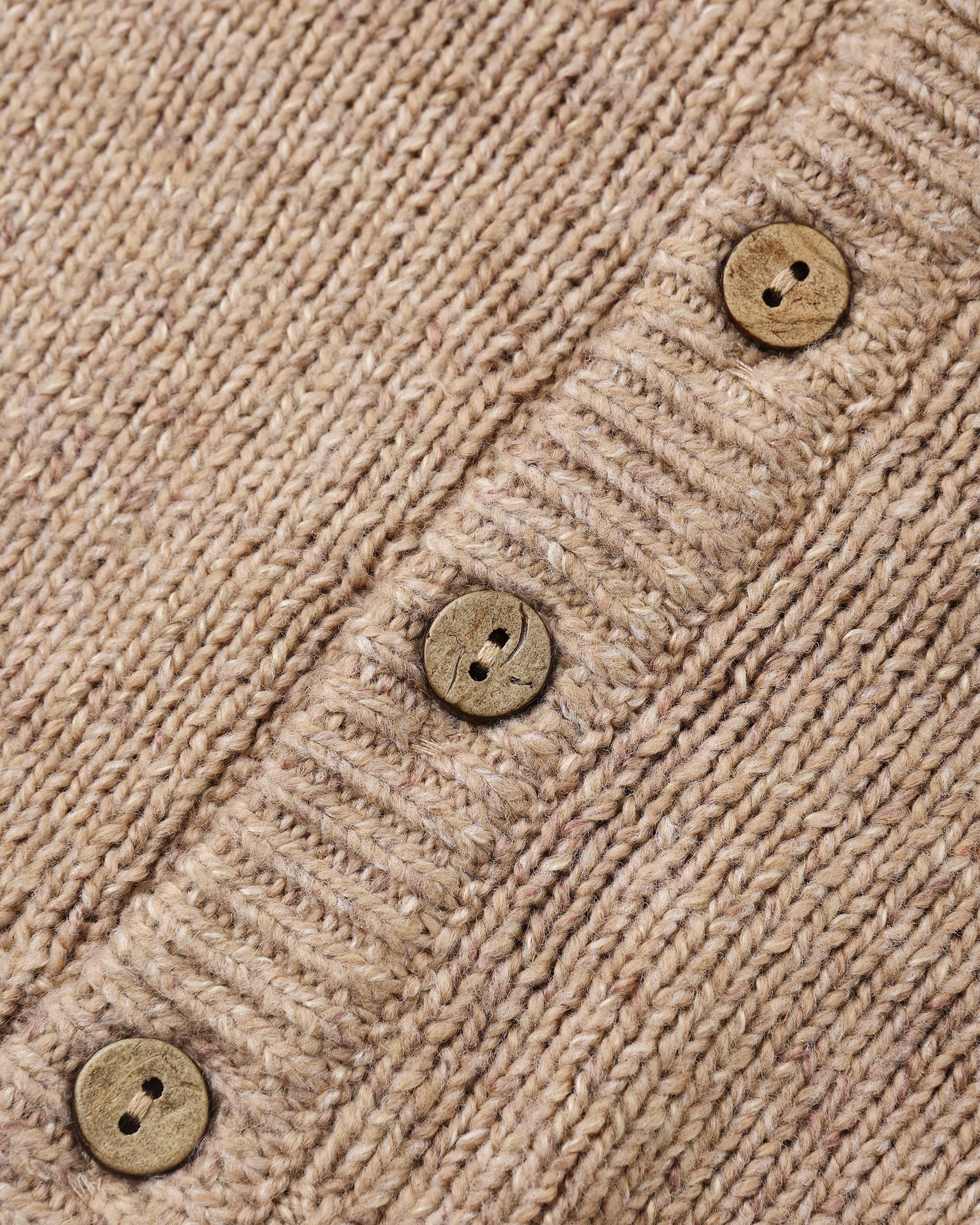 Close-up of a beige knit cardigan or sweater showing the ribbed texture and three round wooden buttons.