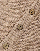 Close-up of a beige knit cardigan or sweater showing the ribbed texture and three round wooden buttons.
