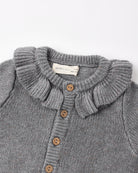 Close-up of a gray ribbed knit cardigan sweater with a ruffled Peter Pan collar and brown buttons, showing a brand label that reads 'QUINCY MART'.