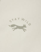 Close-up of a light cream fabric with a muted gray printed logo featuring the words 'STAY WILD' and a running fox silhouette.