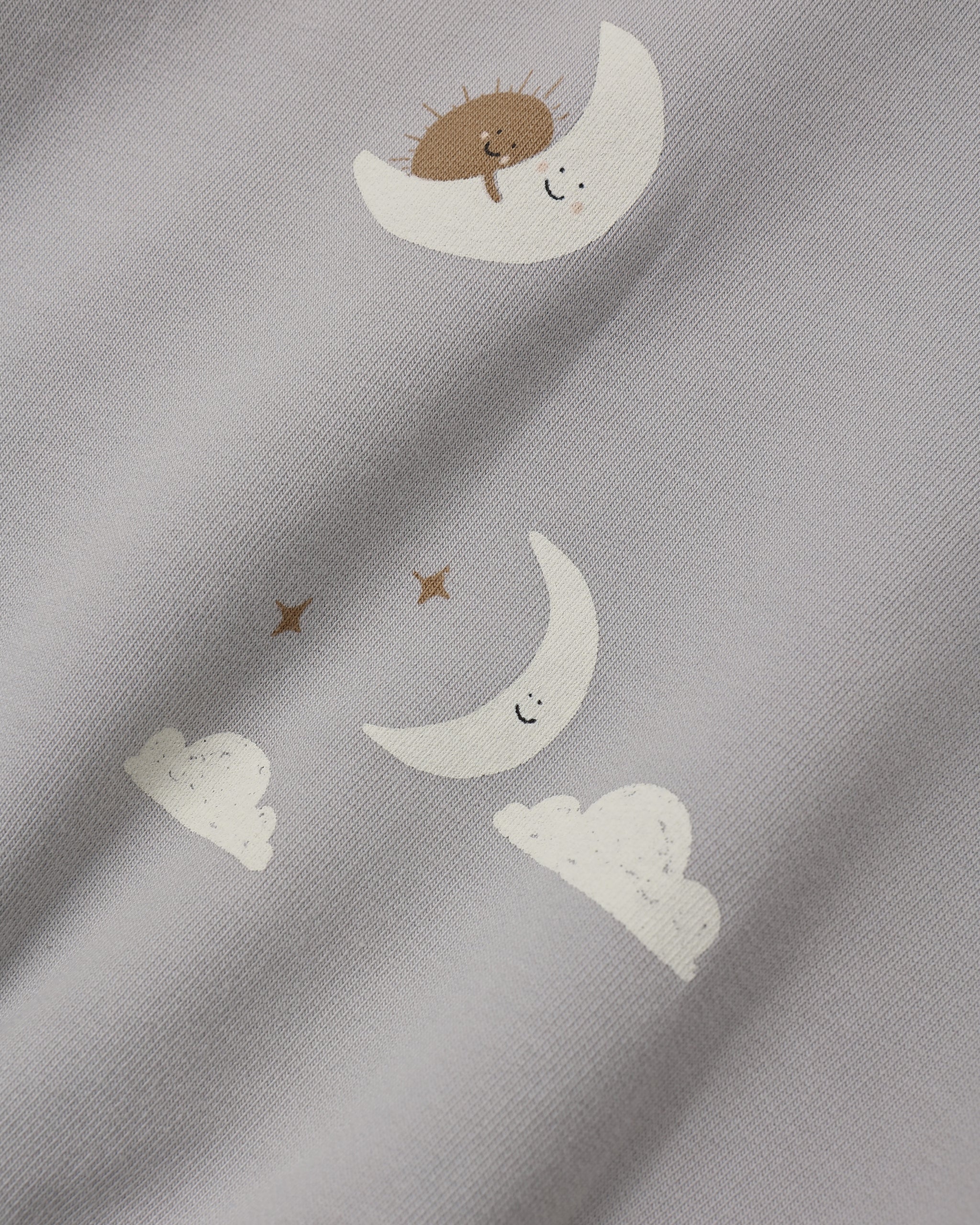 Close-up of a light gray fabric with a whimsical print of white crescent moons, small white clouds, and brown stars, each with a simple smiling face.