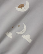 Close-up of a light gray fabric with a whimsical print of white crescent moons, small white clouds, and brown stars, each with a simple smiling face.
