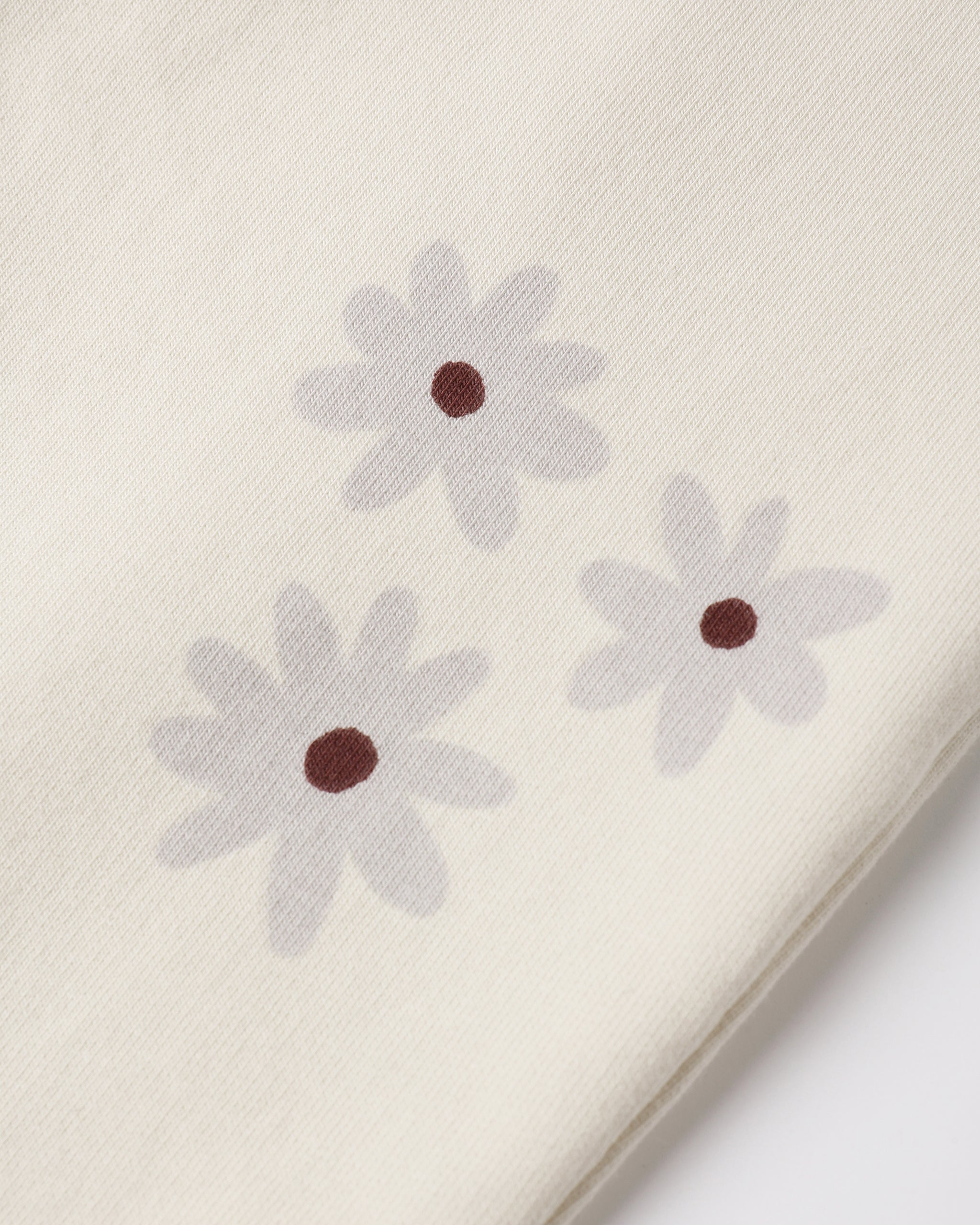 Close-up of a cream-colored fabric with three light gray daisy flowers printed on it, each with a small dark brown center.