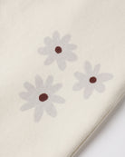 Close-up of a cream-colored fabric with three light gray daisy flowers printed on it, each with a small dark brown center.