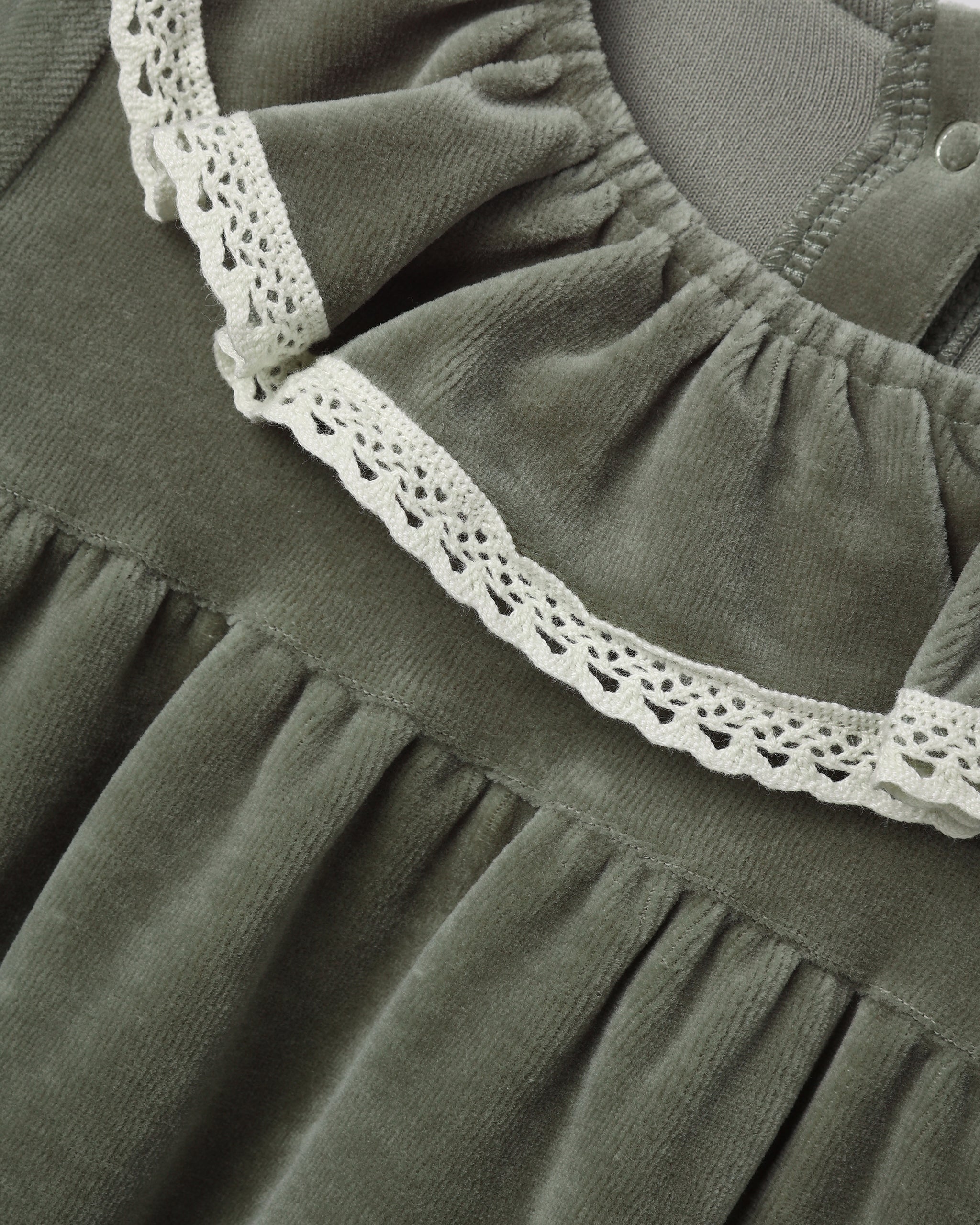 Close-up of a long-sleeve spruce green velour baby dress featuring a ruffled collar edged with delicate white lace.