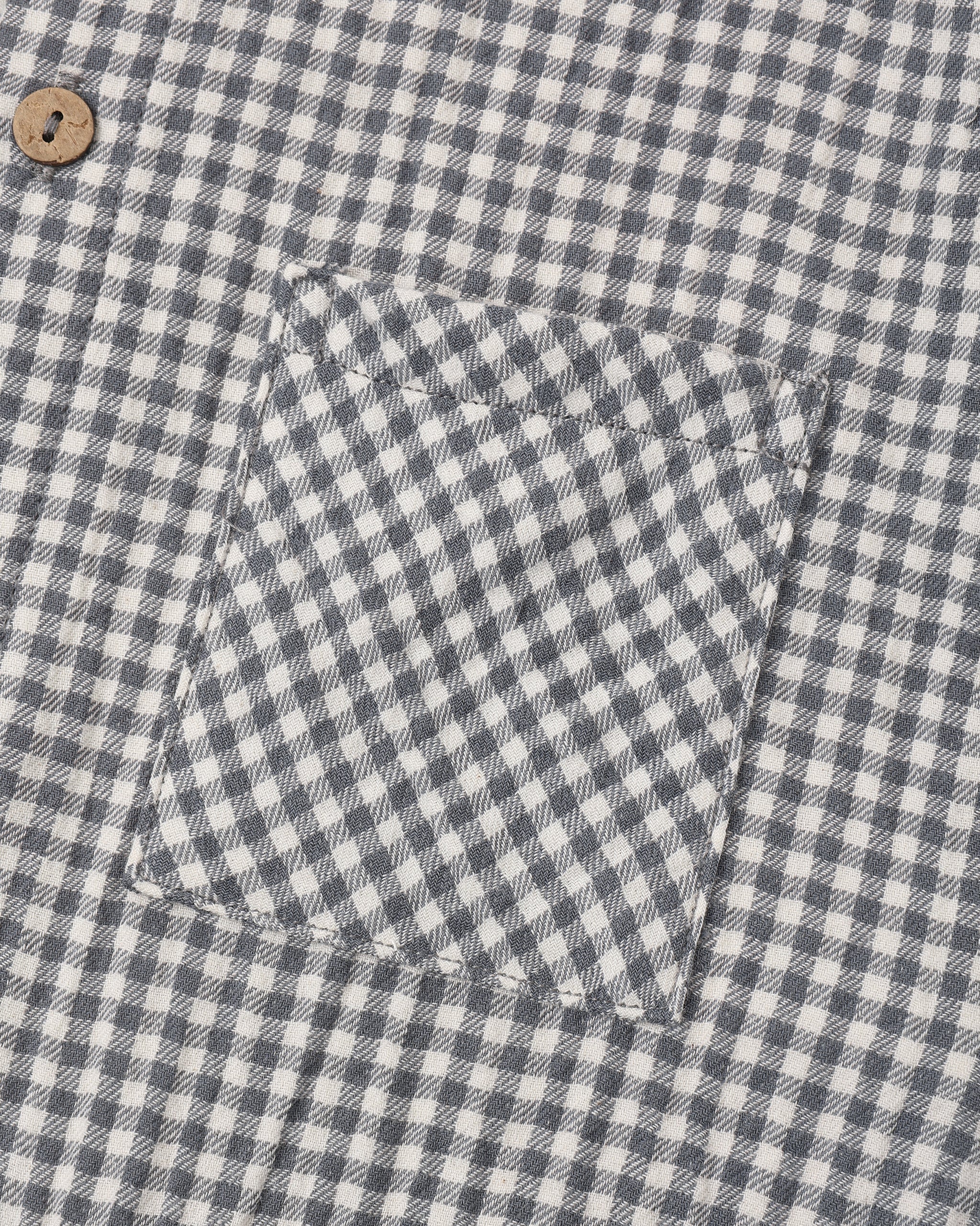 Close-up of a gingham patterned fabric, likely a shirt or jacket, featuring a chest pocket and a single wooden button.