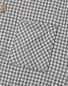Close-up of a gingham patterned fabric, likely a shirt or jacket, featuring a chest pocket and a single wooden button.