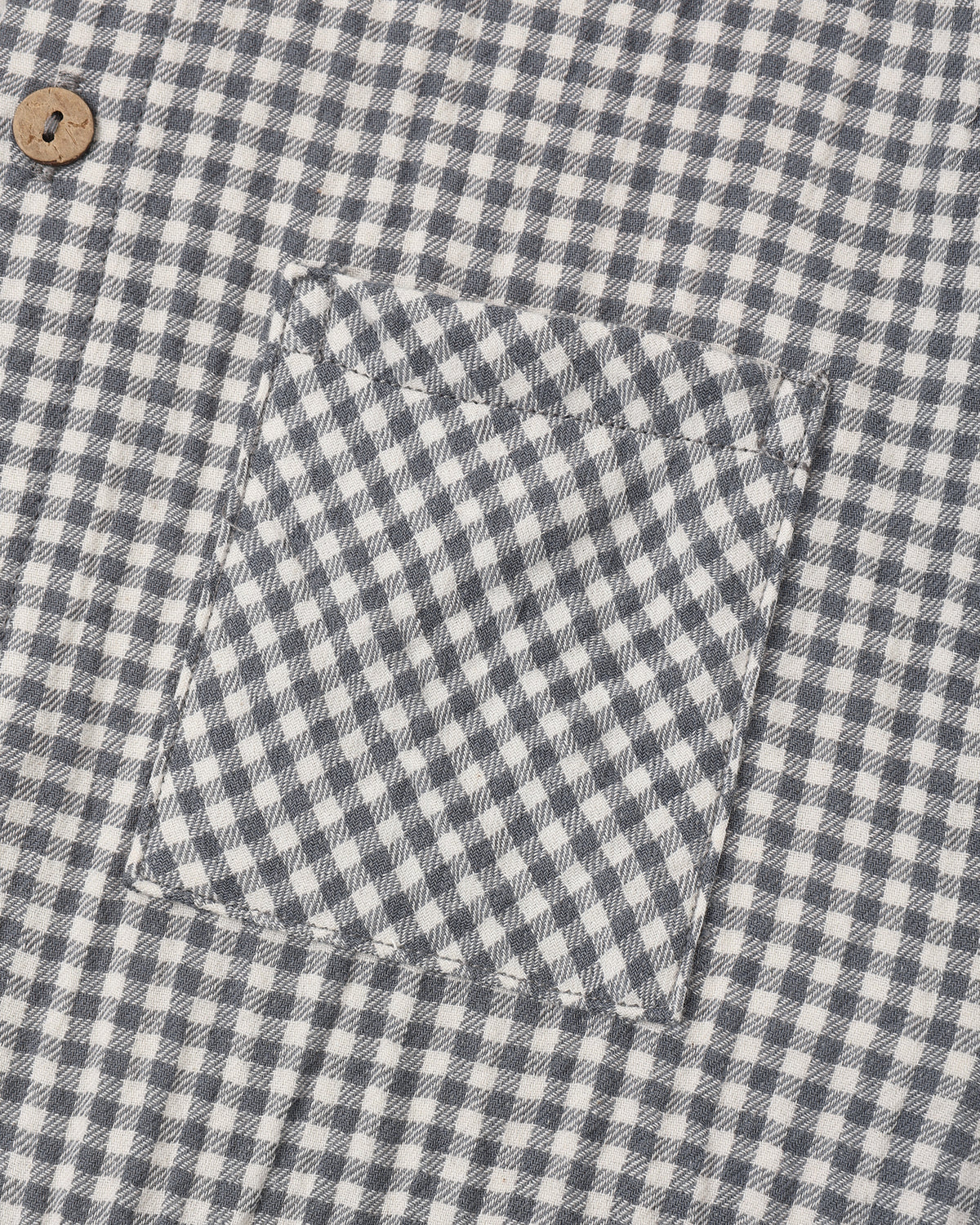 Close-up of a gingham patterned fabric, likely a shirt or jacket, featuring a chest pocket and a single wooden button.