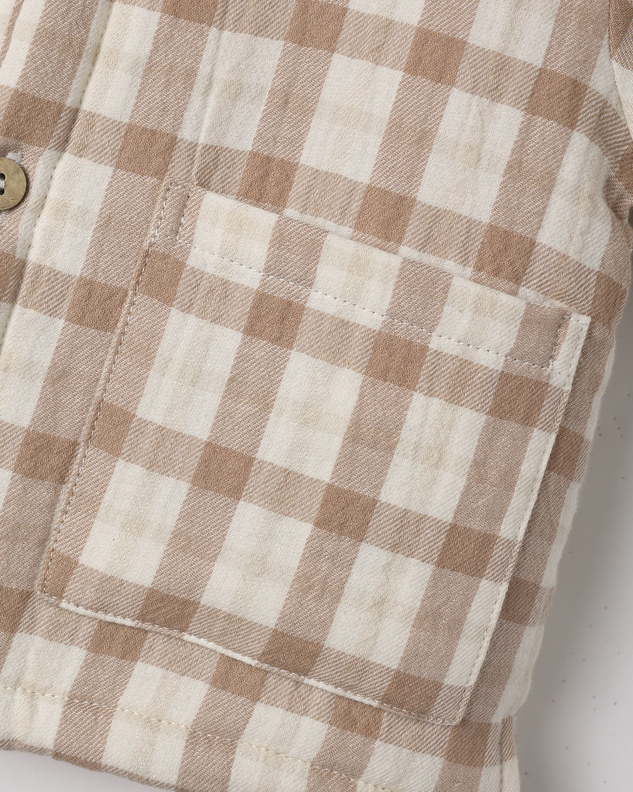 Close-up of a beige and off-white gingham plaid fabric with a stitched pocket and a partial wooden button.
