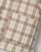 Close-up of a beige and off-white gingham plaid fabric with a stitched pocket and a partial wooden button.