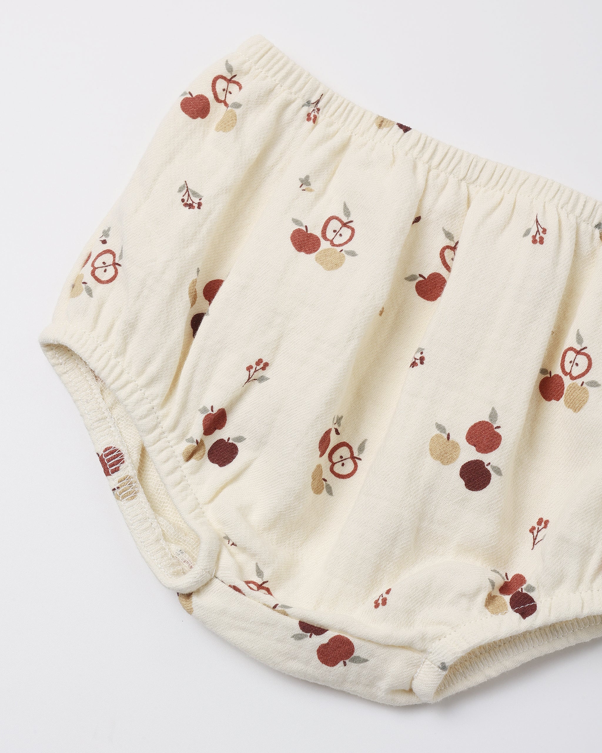 Cream-colored cotton diaper cover with a red and brown apple print, shown on a plain white background.