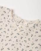A cream-colored children's pointelle top featuring an all-over small floral print and a delicate bow detail at the neckline