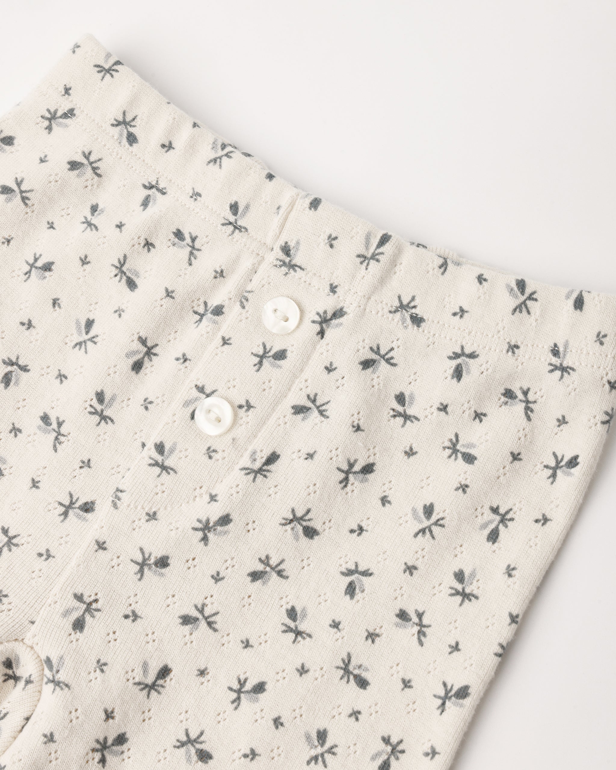 A pair of cream-colored pointelle cotton baby leggings featuring a delicate ditsy floral print and decorative front buttons