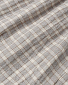 A close-up of a plaid fabric with a gray and off-white checkered pattern and thin brown intersecting lines.