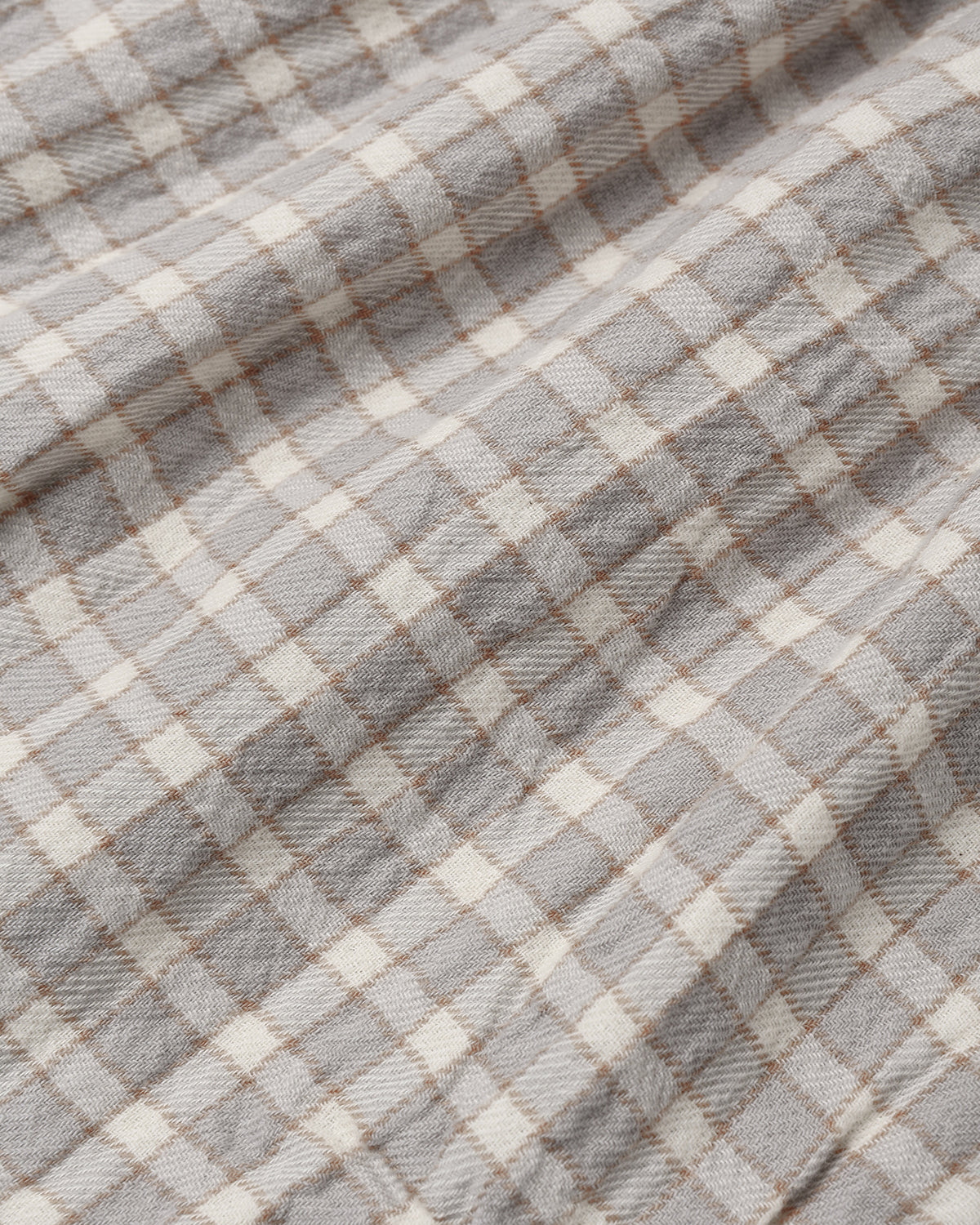 A close-up of a plaid fabric with a gray and off-white checkered pattern and thin brown intersecting lines.