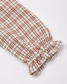 Close-up of a long-sleeve baby dress in a red, white, and tan Christmas plaid pattern, featuring a smocked cuff with a ruffled trim.