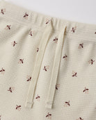 Close-up of a cream-colored waffle-knit fabric with a small brown and dusty pink floral print, featuring a matching cream drawstring waist.