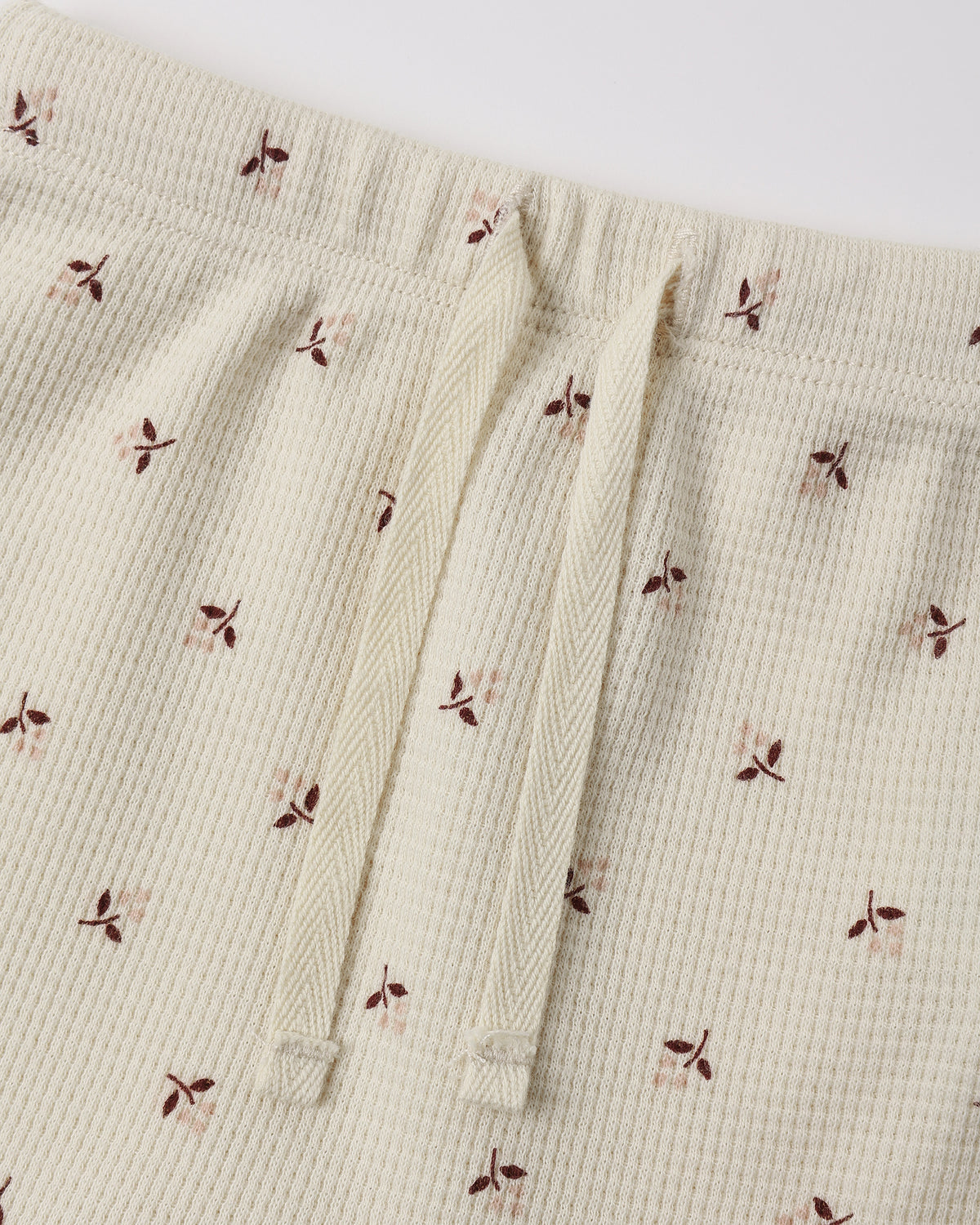 Close-up of a cream-colored waffle-knit fabric with a small brown and dusty pink floral print, featuring a matching cream drawstring waist.