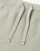 Close-up of a light sage green textured knit garment, showing two matching drawstrings against a white background.