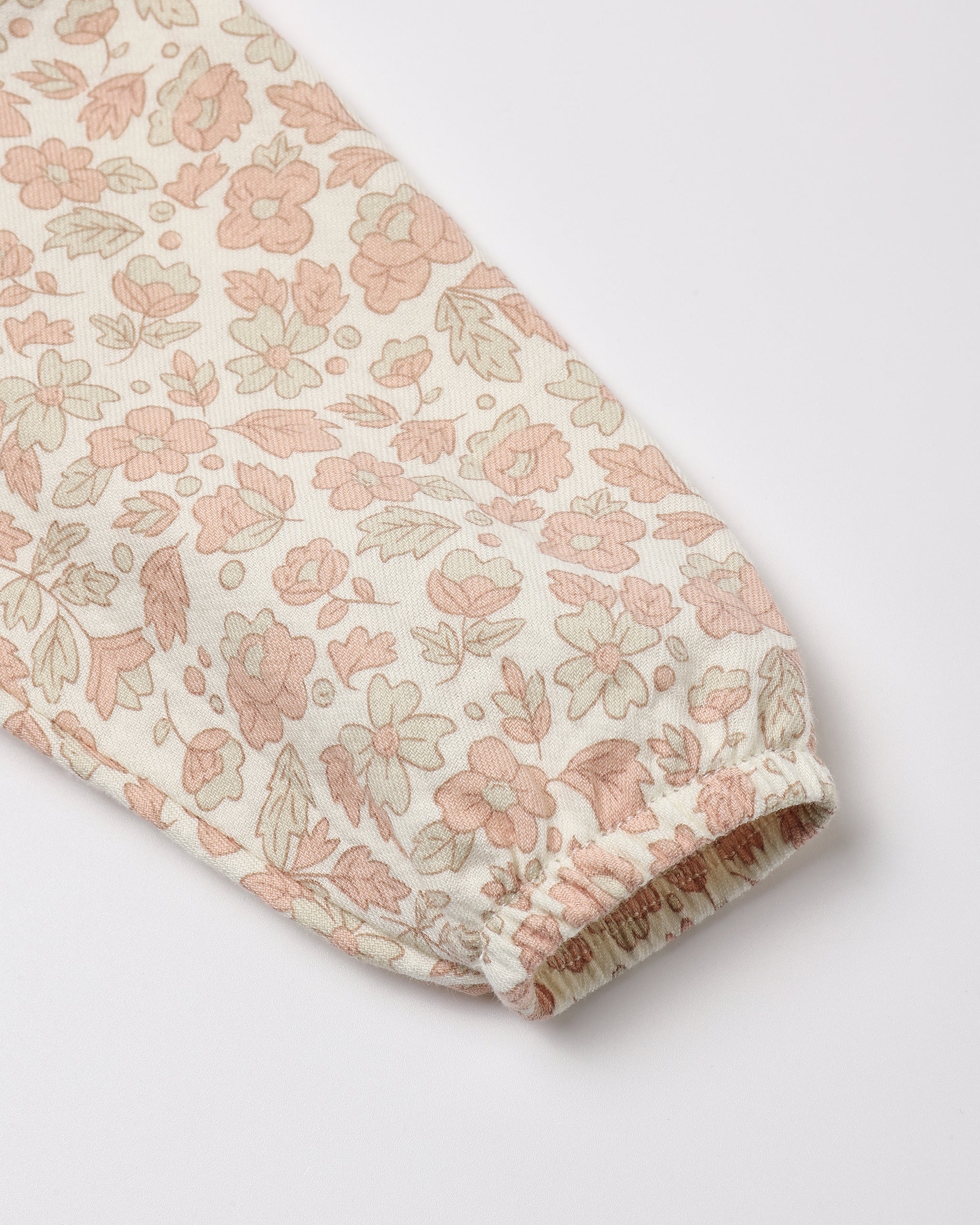 A close-up of a long sleeve featuring an all-over delicate floral and leaf print in soft pink and muted green on an off-white background, finished with a gathered elastic cuff.