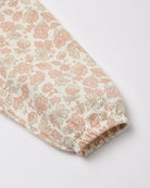 A close-up of a long sleeve featuring an all-over delicate floral and leaf print in soft pink and muted green on an off-white background, finished with a gathered elastic cuff.
