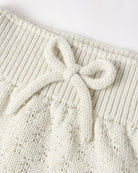 Close-up of a cream-colored knit garment featuring a textured cable-knit pattern and a matching knotted bow detail at the waistband.