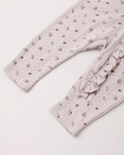 Close-up of a baby or toddler long-sleeve romper or pajama top in a pale blush pink eyelet fabric with a small scattered floral print, featuring a ruffled trim detail on the side.