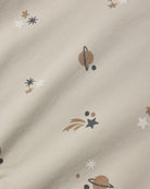 A close-up of a cream-colored fabric with a printed space theme, featuring planets, stars, and shooting stars in brown, white, and dark gray.