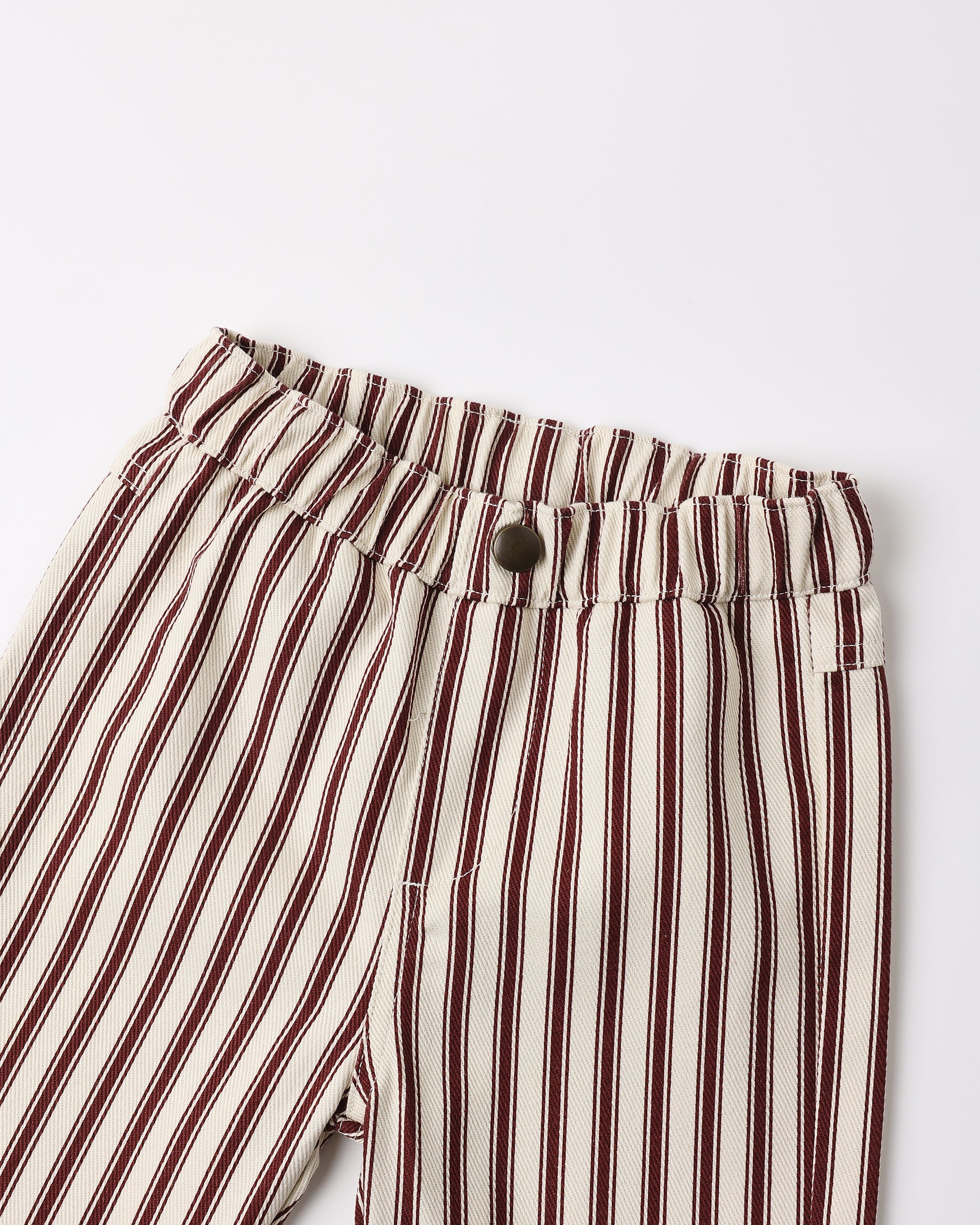 Close-up of striped trousers with vertical dark red and brown stripes on an off-white base, featuring an elastic waistband and a single dark button closure.