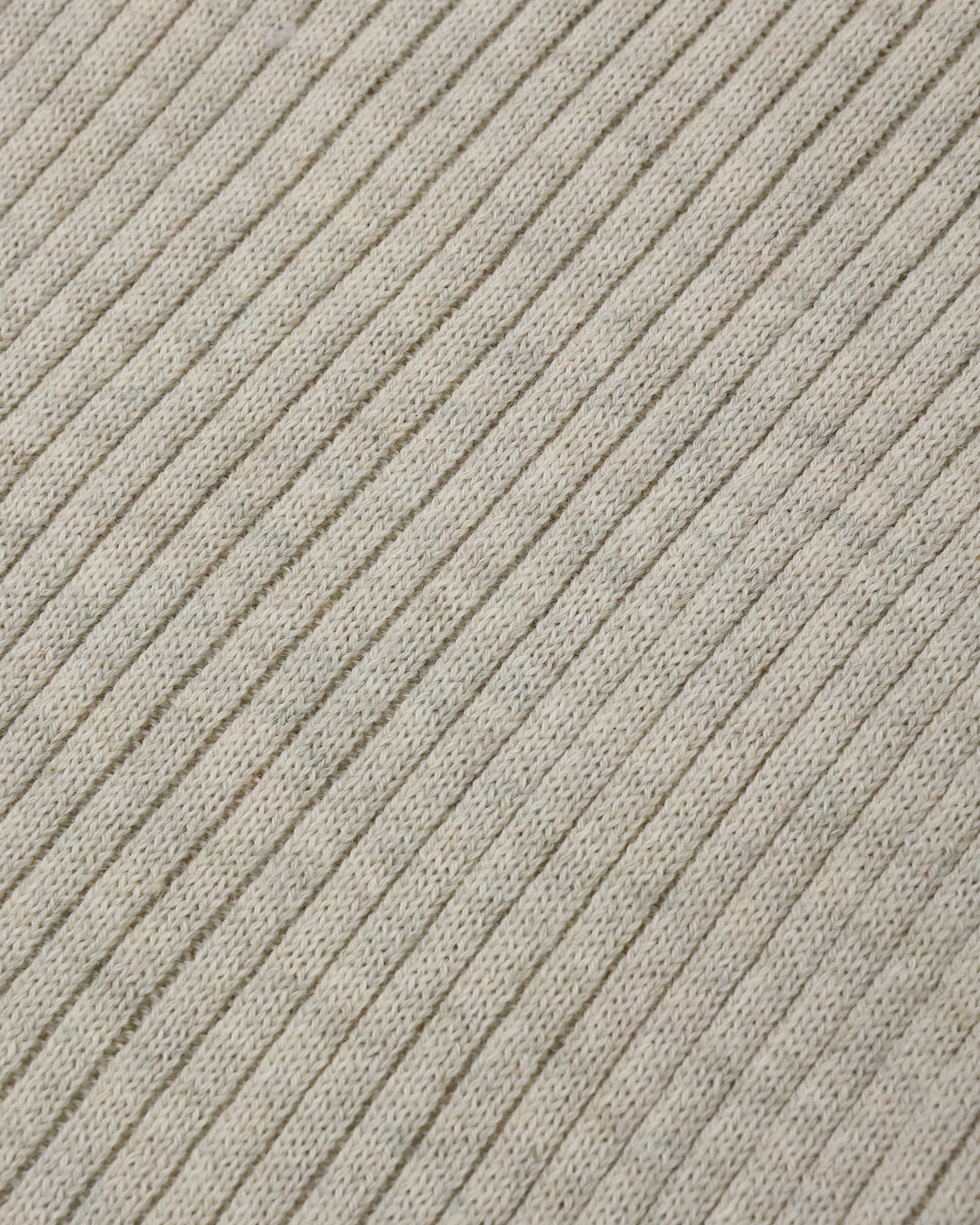 Close-up of a ribbed knit fabric in a light warm gray or oatmeal tone, showing the texture and pattern of the knit stitches.