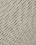 Close-up of a ribbed knit fabric in a light warm gray or oatmeal tone, showing the texture and pattern of the knit stitches.