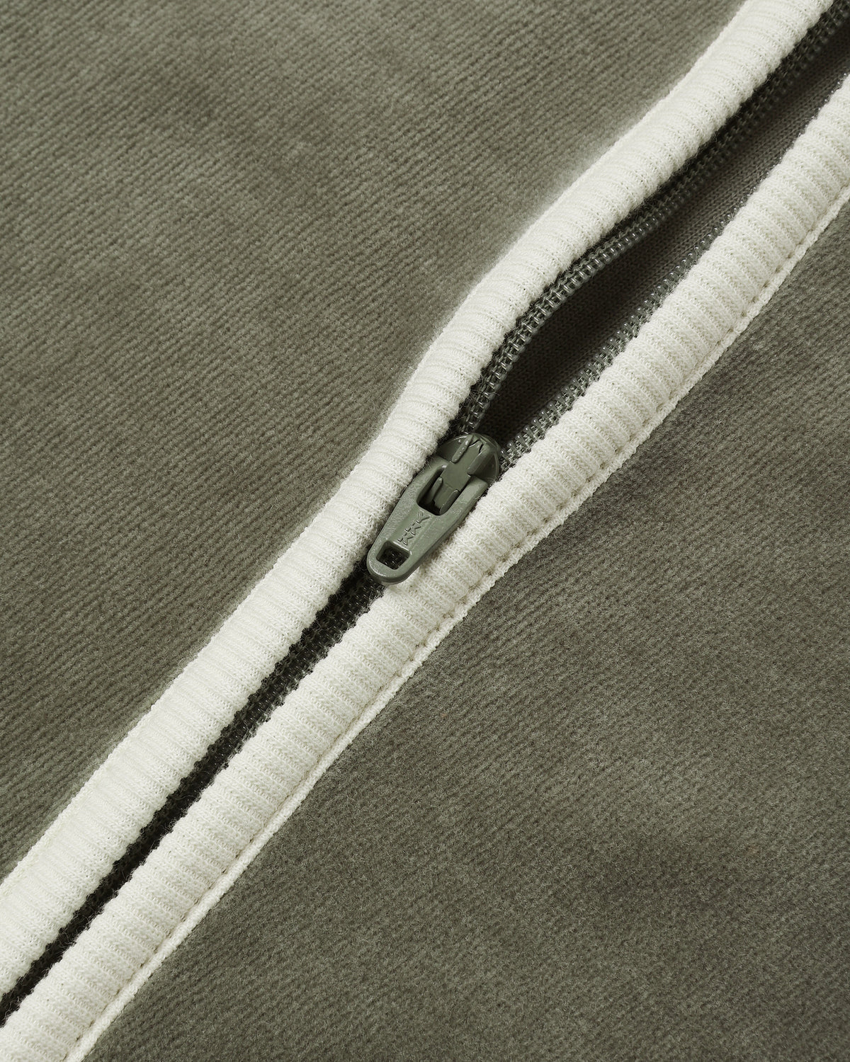 Close-up view of the diagonal white zipper and soft texture of the spruce green velour baby jumpsuit.