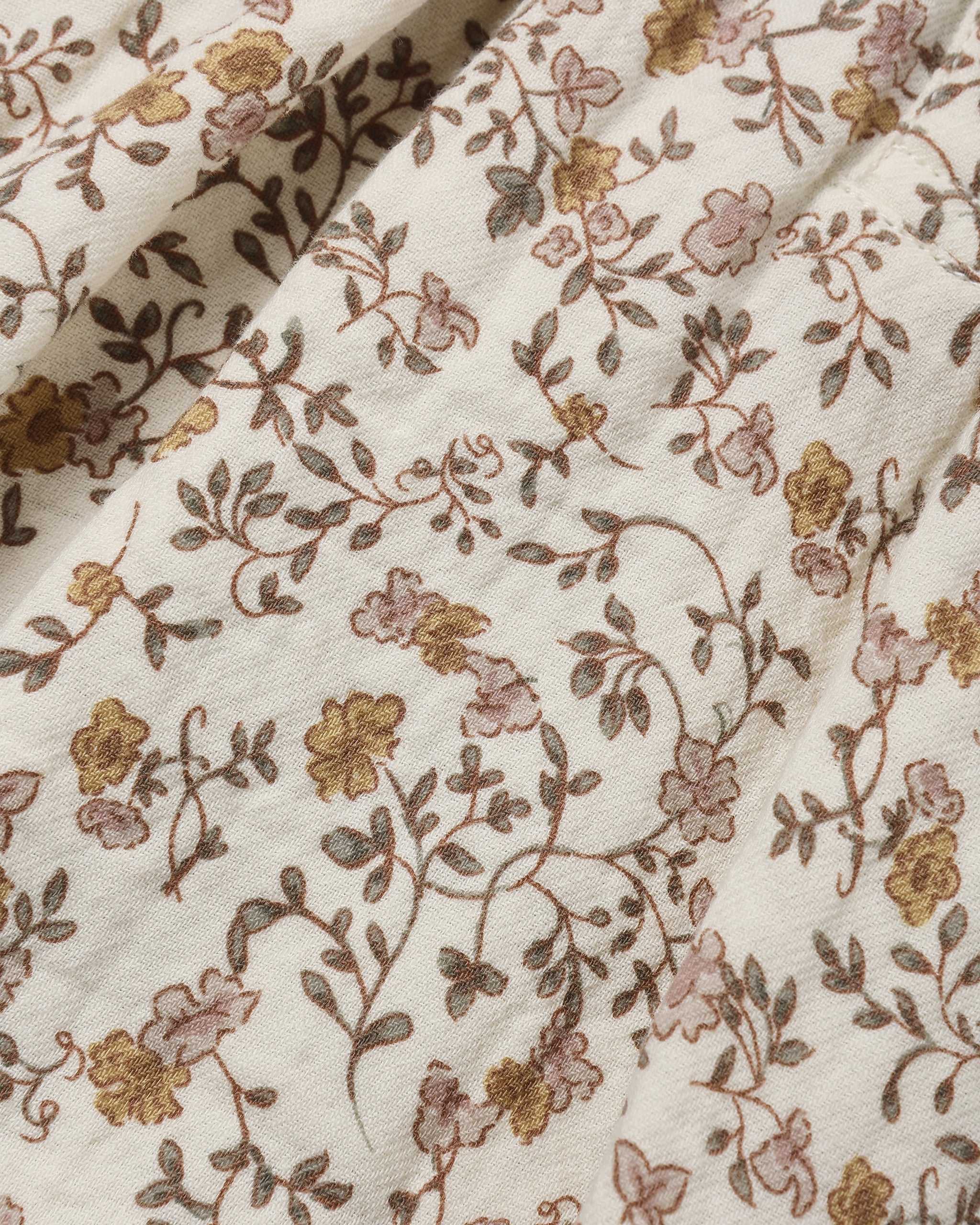 A close-up of a cream-colored fabric with an intricate floral vine pattern in muted brown, dusty pink, and mustard yellow.