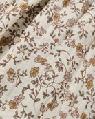 A close-up of a cream-colored fabric with an intricate floral vine pattern in muted brown, dusty pink, and mustard yellow.