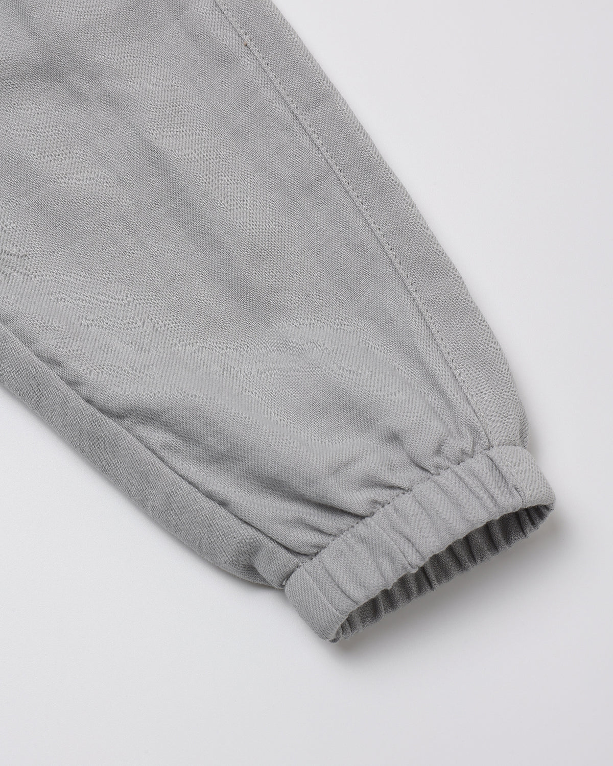 Close-up of a light gray fabric sleeve or cuff with an elastic gathered hem, shown on a plain light background.