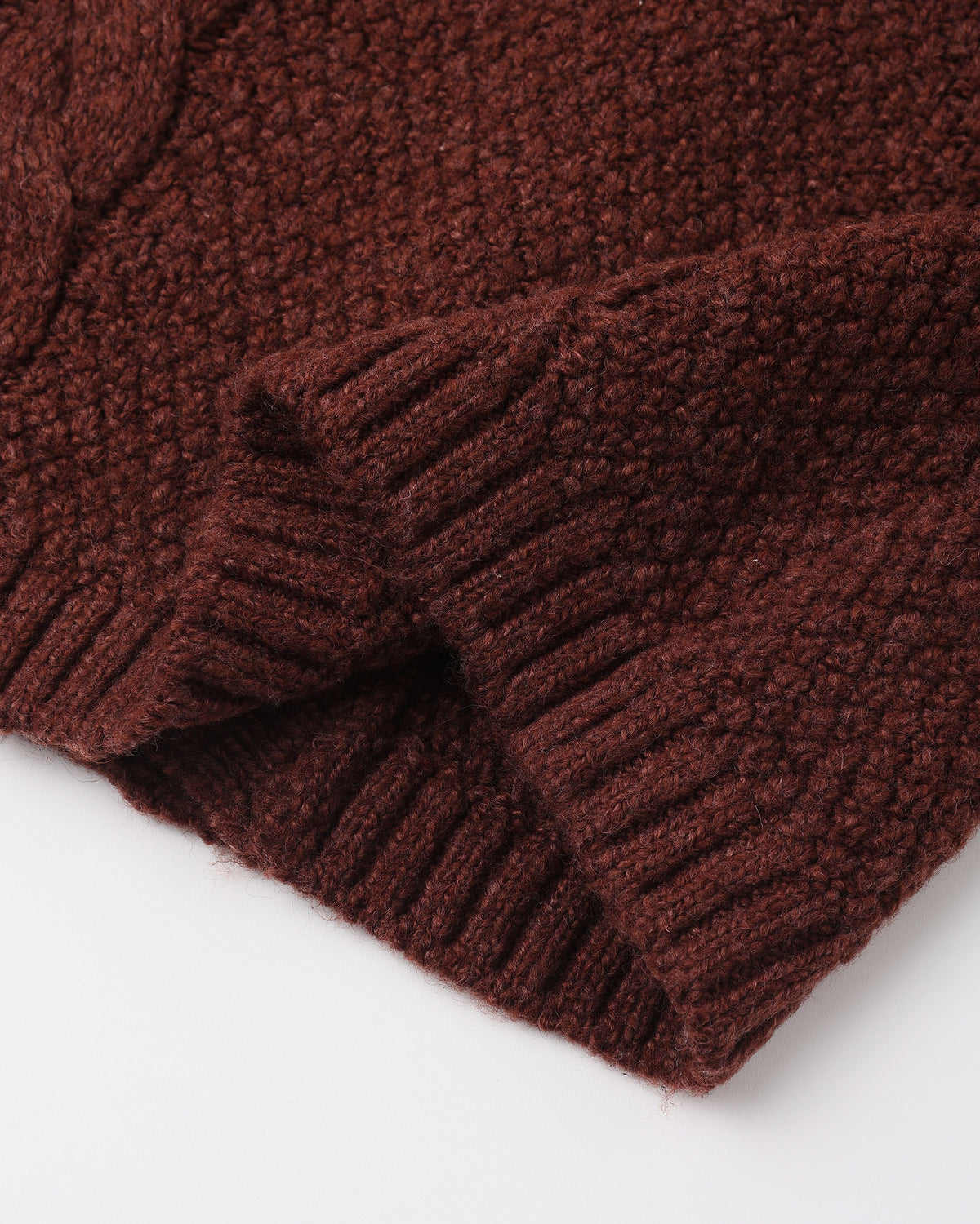 Close-up of a dark brown chunky knit fabric with a ribbed cuff, shown against a plain white background.