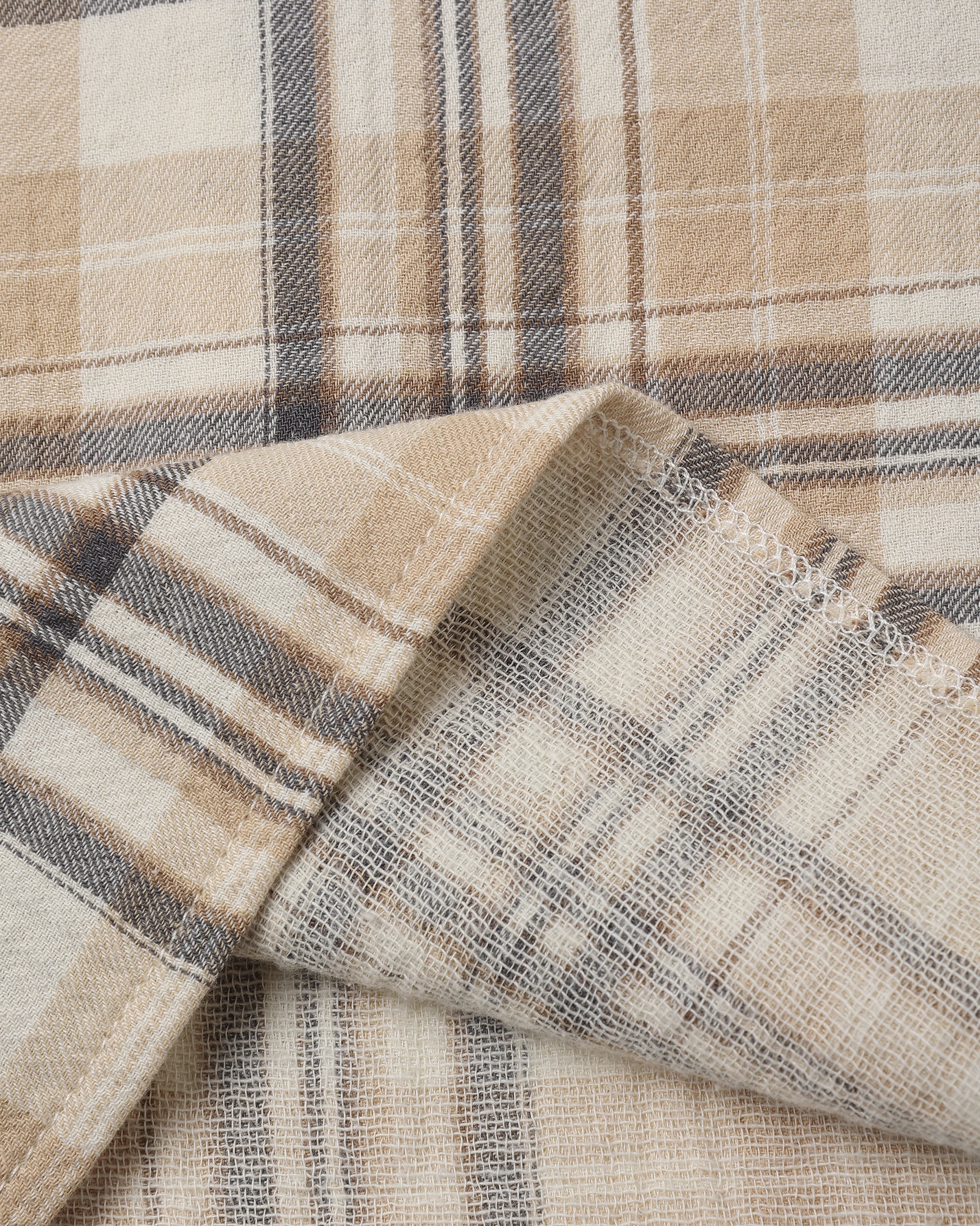 A close-up of a plaid fabric with a warm beige and cream base, accented by brown and gray stripes.