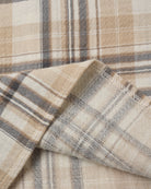 A close-up of a plaid fabric with a warm beige and cream base, accented by brown and gray stripes.