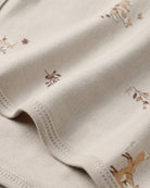 Close-up of a cream-colored knit fabric with a delicate print of small brown and tan woodland animals and leaves, showing the fine knit texture and neat stitching.
