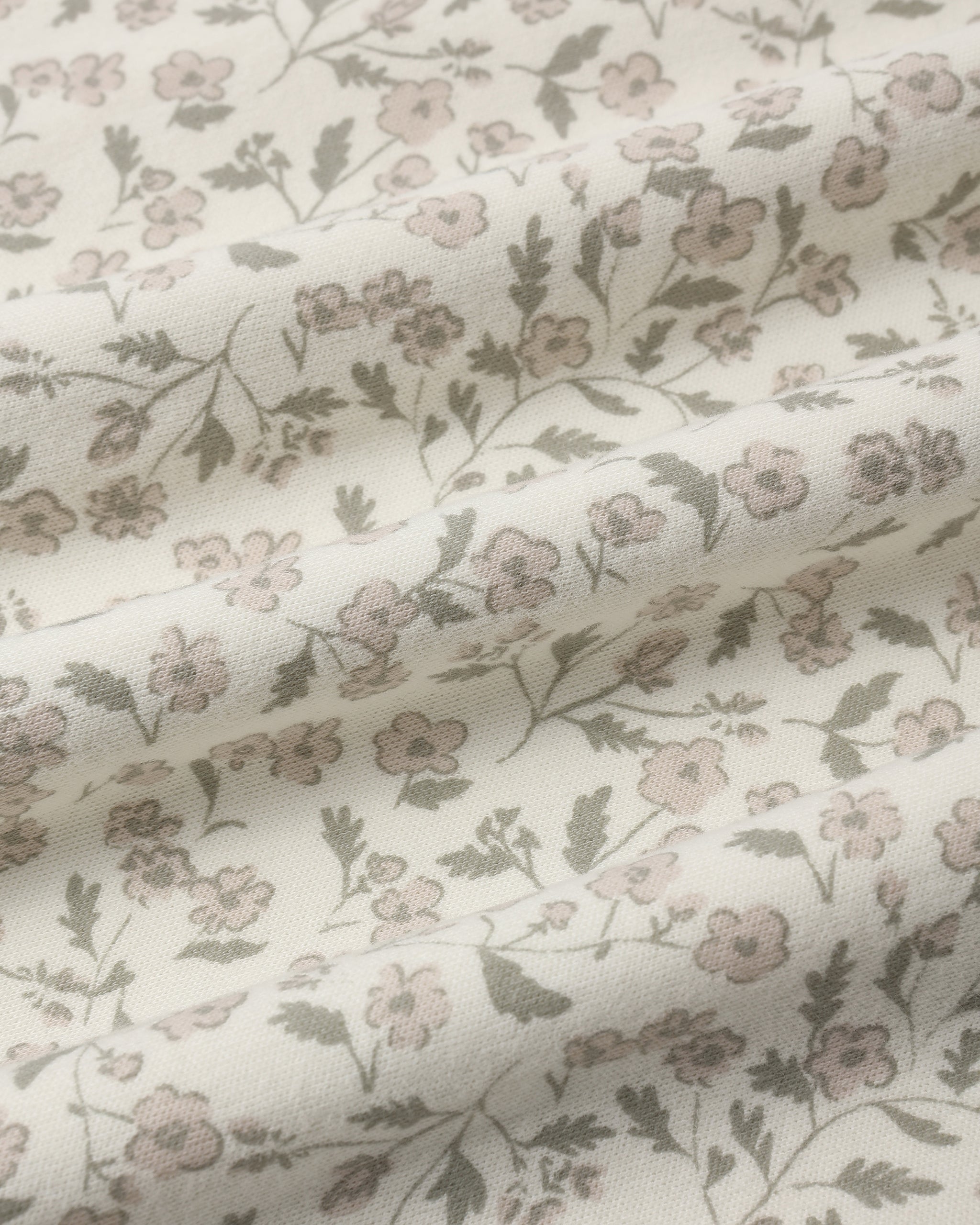 A close-up of a draped fabric with a delicate floral pattern in muted pink and olive green on an off-white background.